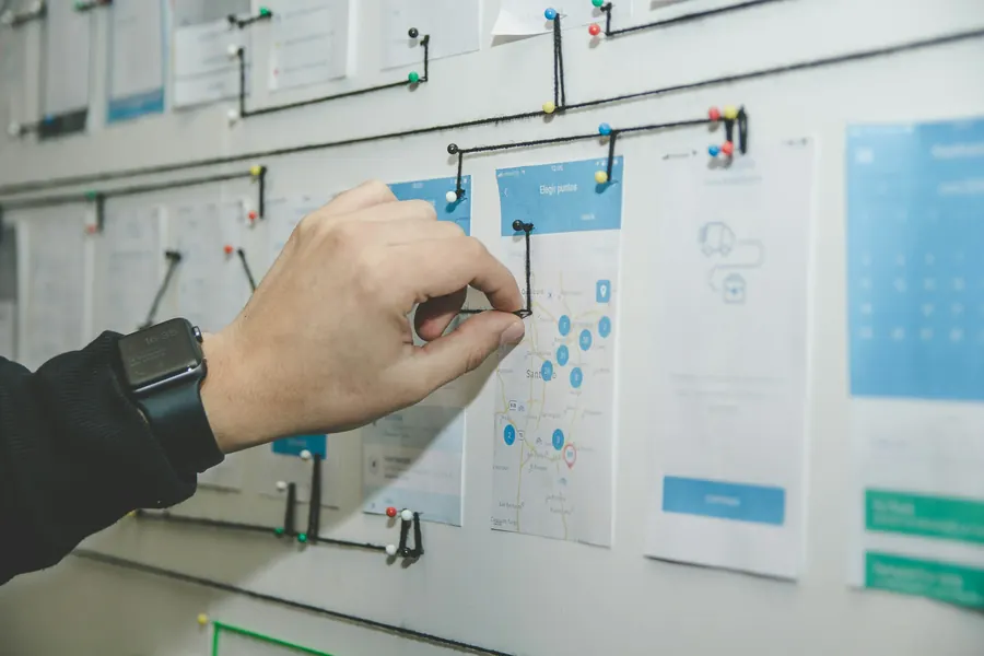 A hand pinning cards and thread onto a wall map of connected steps.