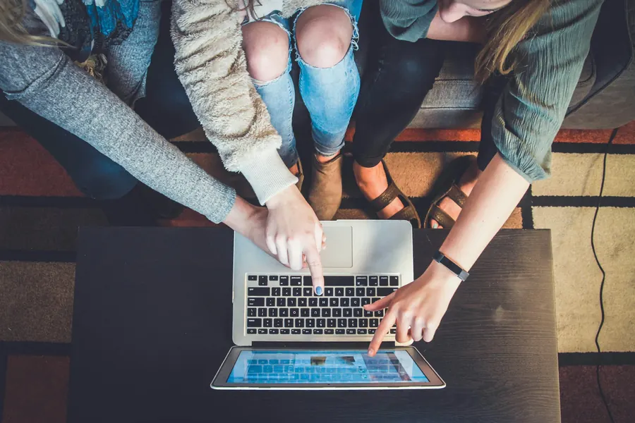 Three people around one laptop, pointing at the screen together.